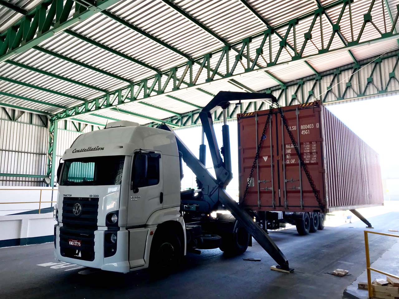 Caminhão com braço hidraulico descarregando container de carga